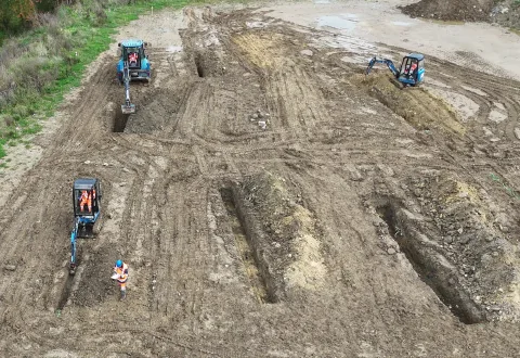 Vue aérienne du plateau technique de Warcq : quatre mini-pelles ouvrant des tranchées, un formateur au sol