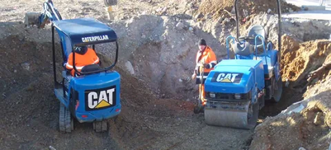 Mini-pelle et compacteur tandem au travail dans une tranchée